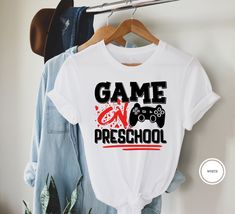 "Game On Preschool Shirt Hi! Welcome to my store, I'm delighted to see you here. My store's main goal is to provide you with premium everyday apparel with the best graphic t-shirts.  DESCRIPTION * Printed and shipped from the USA. * We use state of art printing on soft and quality shirts. * Different size options; crewneck, youth, women's v-neck, toddler, and baby size options.  * Effective customer service and expedited shipping.  * Solid colors are 100% airlume combed and ringspun cotton.  * Heather colors 52/48 cotton/polyester. * Shoulder taping. Side-seamed. Fitted at bicep. Tear-away label. 4.2 oz. SIZES AND COLORS * Please refer to the size charts for measurements before placing an order. * You can compare our numbers to one of your favorite shirts to make sure. * Unisex shirts are Game Day Cotton T-shirt For End Of School Year, Cotton T-shirt For Game Day, End Of School Year, School Spirit Cotton Shirt With Heat Transfer Vinyl, White Slogan Shirt For School, White Cotton Gamer T-shirt, School Spirit Shirt With Letter Print For Streetwear, School T-shirt With Heat Transfer Vinyl, Cotton T-shirt With Heat Transfer Vinyl For School, School Spirit Cotton Shirt With Slogan