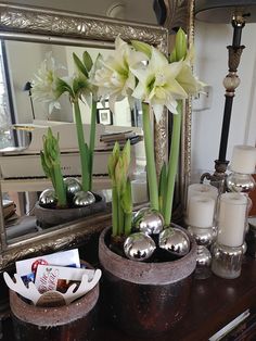 some white flowers are sitting in pots on a dresser next to candles and a mirror