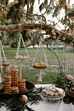 desserts and pastries are displayed on trays under a tree with hanging macaroons