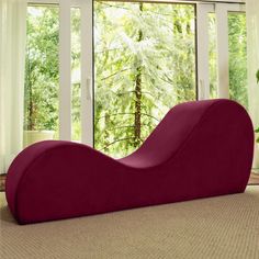 a large red chaise lounger sitting in front of a window next to a potted plant