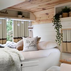 a white bed with pillows and blankets in a bedroom next to a wooden shelf filled with potted plants