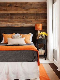 a bed with orange and white pillows on top of it next to a wooden wall