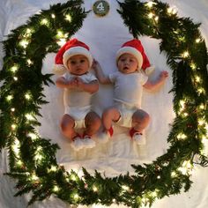 two babies wearing santa hats are laying on a blanket surrounded by christmas wreaths and lights