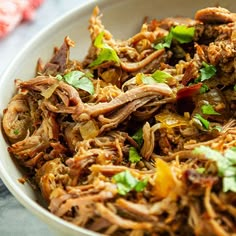 a white bowl filled with shredded meat and garnished with cilantro leaves