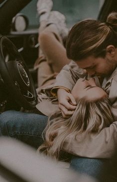 a man and woman sitting in the drivers seat of a car, one is kissing the other's forehead