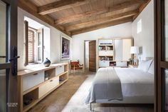 a bedroom with white bedding and wooden ceilinging, along with open windows to the outside