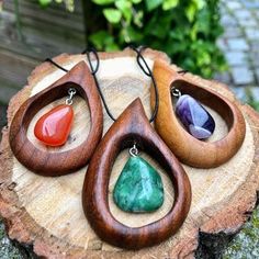 three wooden pendants with different colored stones on them sitting on a piece of wood