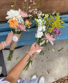 two people holding flowers in their hands on the ground next to a blue wooden bench