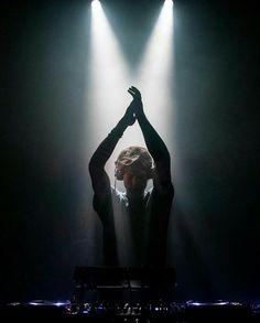 a man standing on top of a stage with his hands in the air and lights behind him