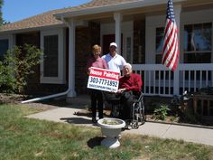 three people standing in front of a house holding a for sale sign