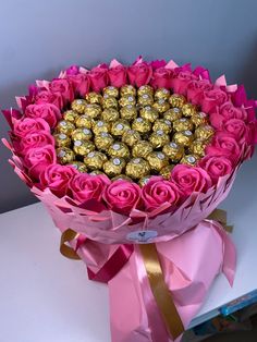 a bouquet of pink roses and chocolates wrapped in pink paper with a gold ribbon