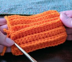 someone crocheting an orange piece of cloth with a pair of scissors in their hands