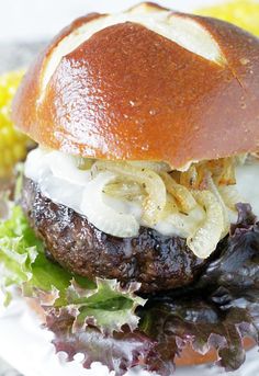 a hamburger with onions, lettuce and cheese on a plate next to corn