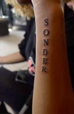 someone has a tattoo on their arm that says sonder in cursive writing