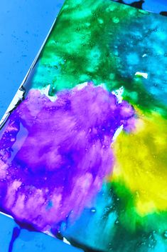 an abstract painting is being made with colored inks and water droplets on a blue surface