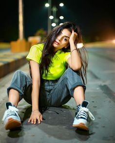 a young woman sitting on the ground with her hands behind her head and looking at the camera