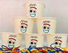 five cups with faces drawn on them and streamers around them, all decorated in different colors