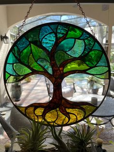 a stained glass window with a tree in the center and two air plants hanging from chains