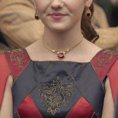 a woman wearing a red and black dress with a gold necklace on her neck is looking at the camera