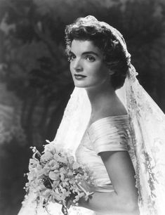 an old black and white photo of a woman in a wedding dress holding a bouquet