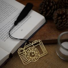 an open book with a camera on it next to a candle and some pine cones