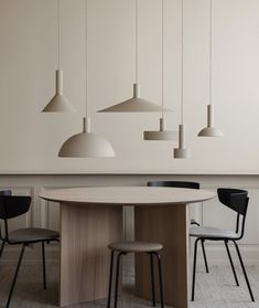 a dining room table with four chairs and three pendant lights hanging from the ceiling above it