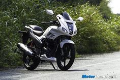 a white motorcycle parked on the side of a road next to tall grass and bushes