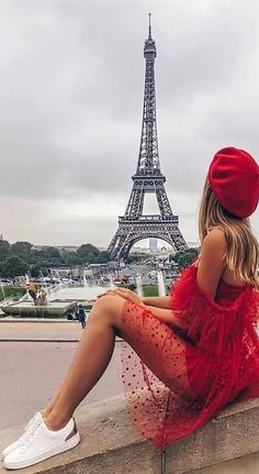 a woman in a red dress and hat sitting on a ledge near the eiffel tower