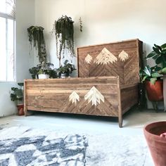 a wooden bed sitting in the middle of a room next to potted plants on top of a rug