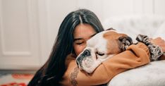 a woman laying on top of a bed with a dog in her lap and she is cuddled up to the pillow