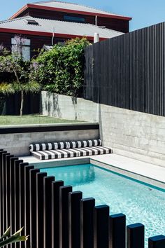 an outdoor swimming pool surrounded by black metal fence and wooden slatted walls with trees in the background