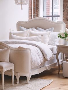 a white bed sitting in a bedroom next to a window with a chandelier