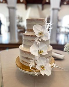 a three tiered cake with white flowers on the top is sitting on a table