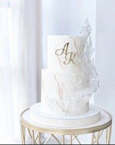 a three tiered wedding cake with white frosting and gold lettering on top, sitting on a stand