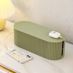 a green speaker sitting on top of a white table next to a lamp and remote control