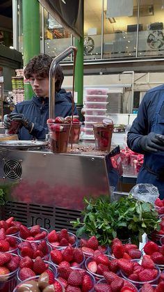 two men working at a fruit stand with strawberries and other fruits on the table