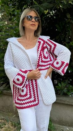 a woman wearing white pants and a red and white crochet jacket is posing for the camera