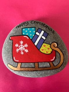 a painted rock with a sleigh and presents on it that says happy christmas