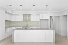 an empty kitchen with white cabinets and counter tops in the middle of it is lit by three pendant lights