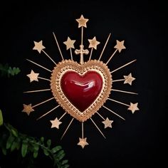 a red heart surrounded by gold stars on a black background with greenery in the foreground