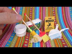 a person is holding two brooms and cleaning supplies on a colorful table cloth with a caution sign in the background