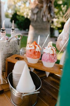 three scoops of ice cream sitting on top of a wooden table next to silver buckets