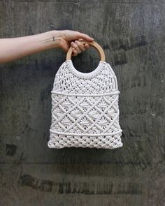 a hand holding a white woven purse on top of a cement wall with a wooden handle