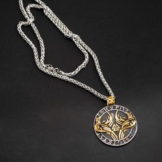 a gold and silver necklace with an intricate design on the front, sitting on a black surface