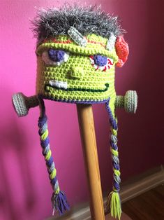 a crocheted monster hat on top of a wooden stick in front of a pink wall