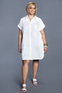 a woman in a white shirt dress posing for the camera with her hands on her hips