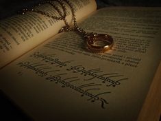 an open book with two gold rings on it and a chain hanging from the pages