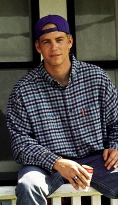 a man sitting on a porch with his hands in his pockets and wearing a hat