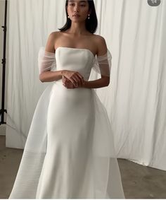 a woman standing in front of a white backdrop wearing a wedding dress with sheer sleeves