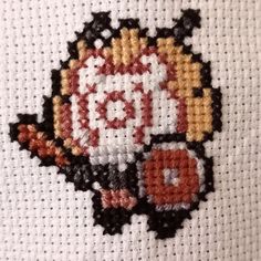 a close up of a cross stitch on a piece of cloth with an orange and black design